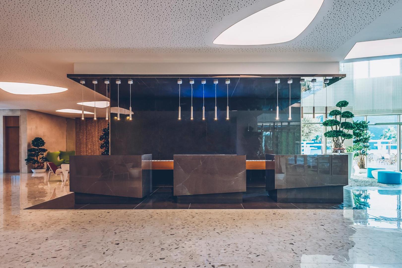 Carine Hotel Kumbor Superior viesnīcas recepcijas zona ar modernu tumša akmens dizainu, stilīgiem gaismekļiem un plašu, gaišu foajē.