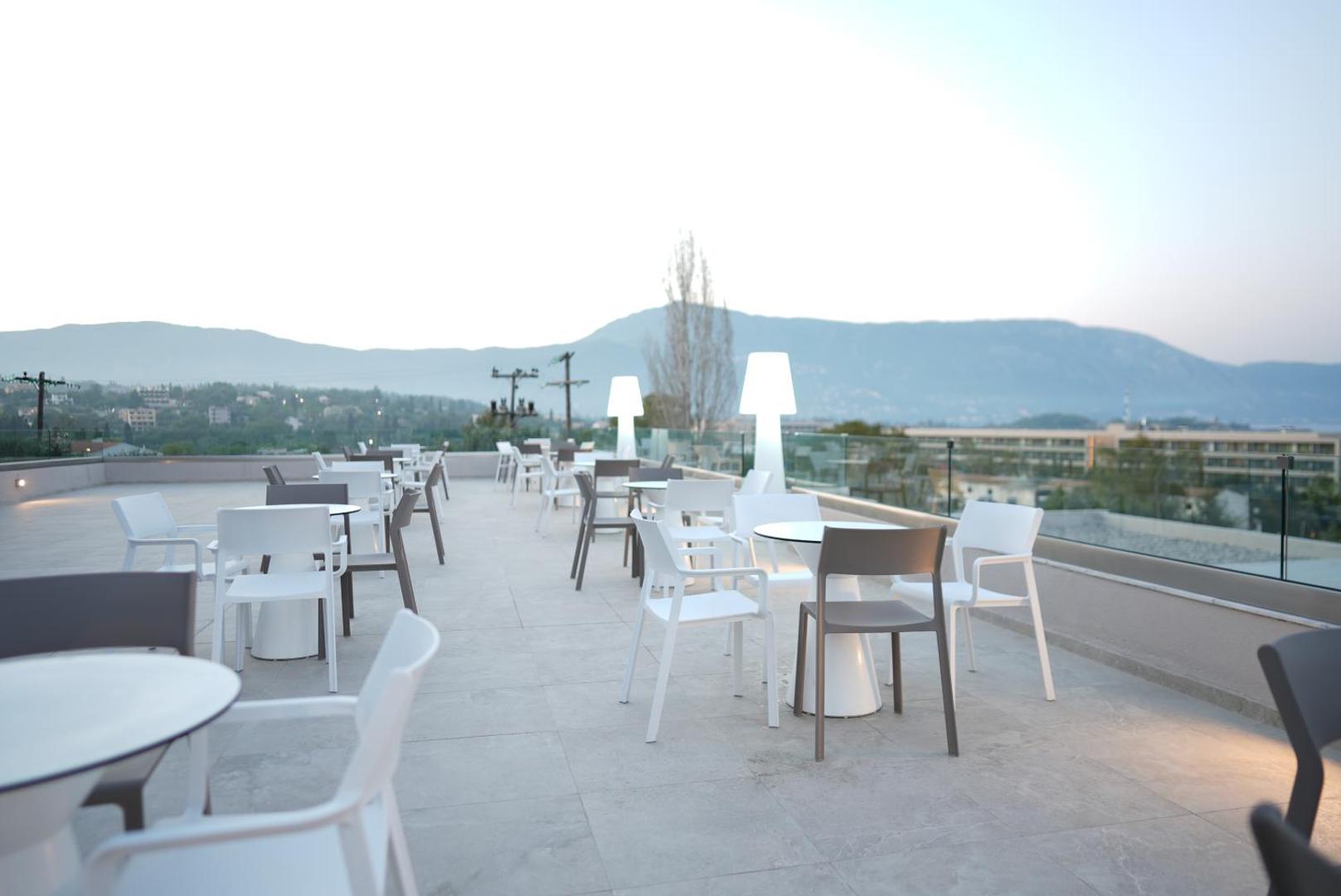Iolida Corfu Resort & Spa jumta terase ar galdiņiem un skatu uz kalniem tālumā, krēslas stundā ar dekoratīvo apgaismojumu