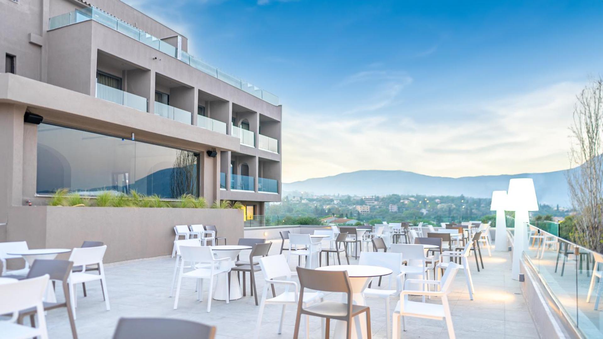 Iolida Corfu Resort & Spa plašā āra terase ar moderniem galdiņiem un krēsliem, no kuras paveras skats uz Korfu ainavu