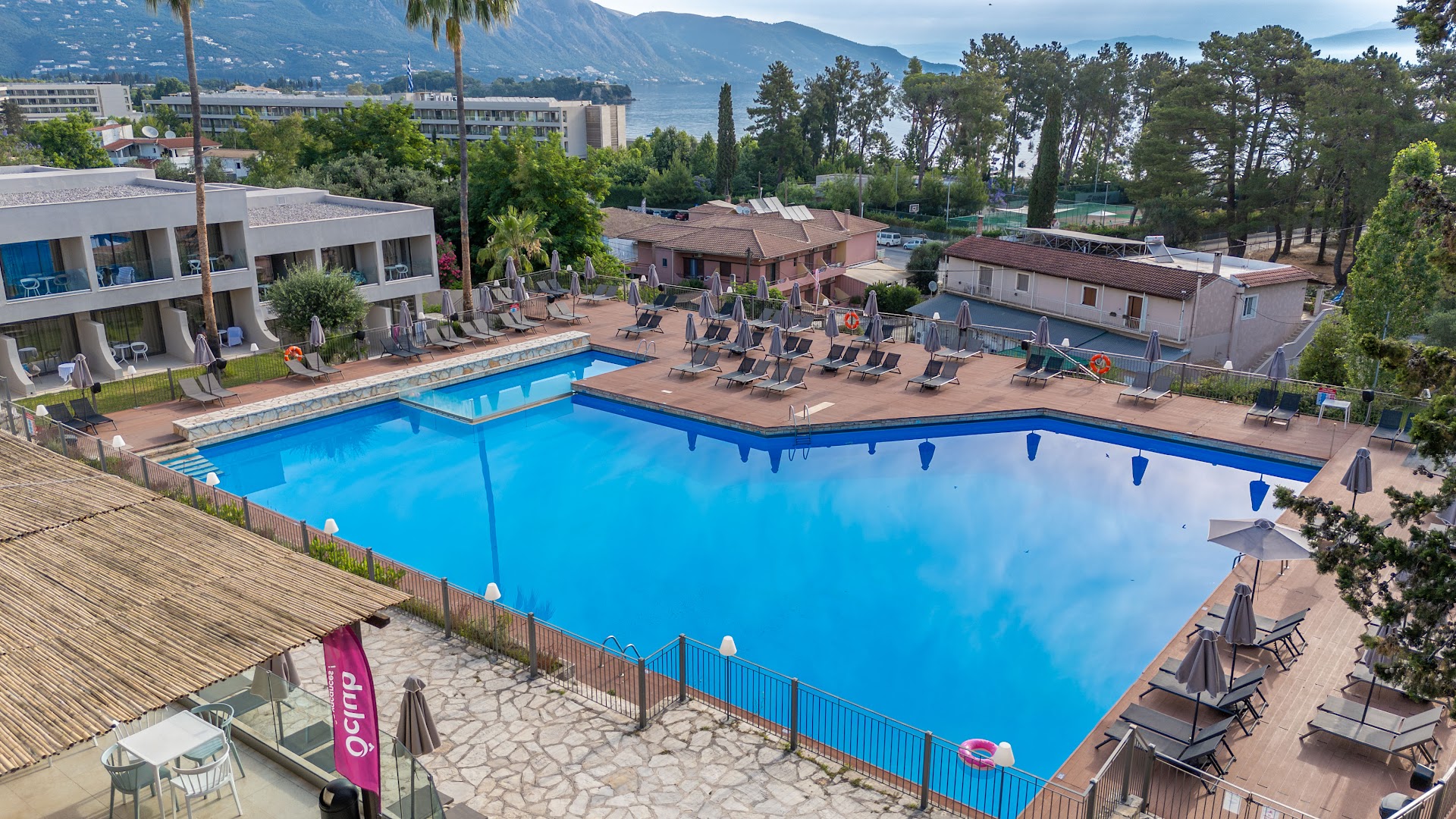 Iolida Corfu Resort & Spa otrs āra baseins ar koka klāju, sauļošanās krēsliem un skatu uz Korfu piekrastes kalniem