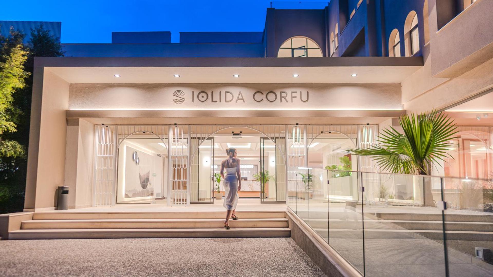 Iolida Corfu Resort & Spa ieeja vakarā ar izgaismotu viesnīcas nosaukumu un modernu stikla fasādi Korfu salā, Grieķijā