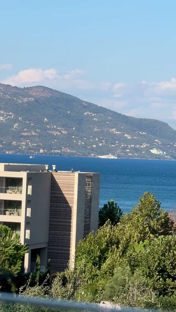 Iolida Corfu Resort & Spa skats no numura balkona uz Jonijas jūru un kalniem Korfu piekrastē ar jahtu tālumā