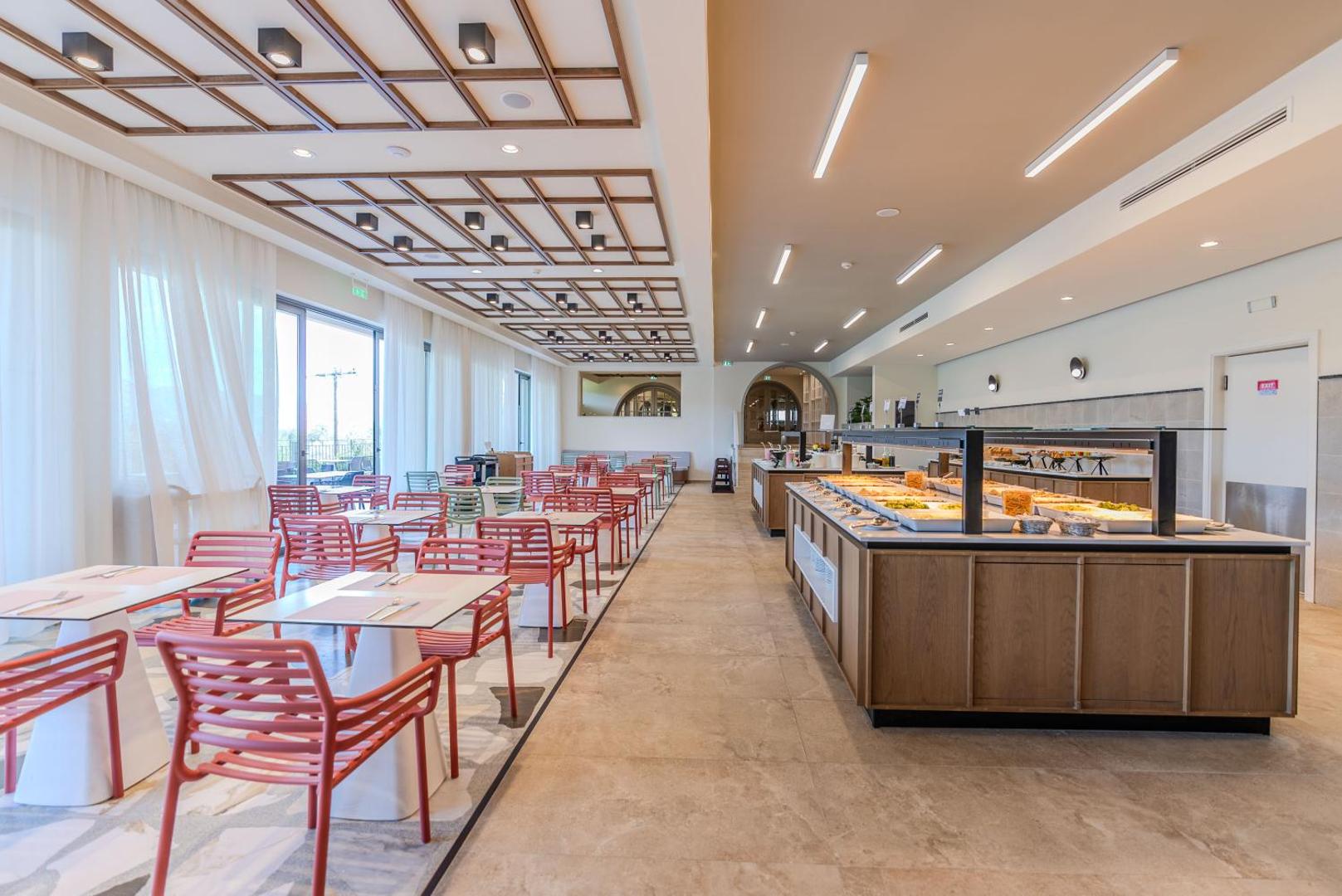 Iolida Corfu Resort & Spa galvenais restorāns ar modernu interjeru, koka griestu dekorācijām un bufetes tipa ēdināšanas zonu
