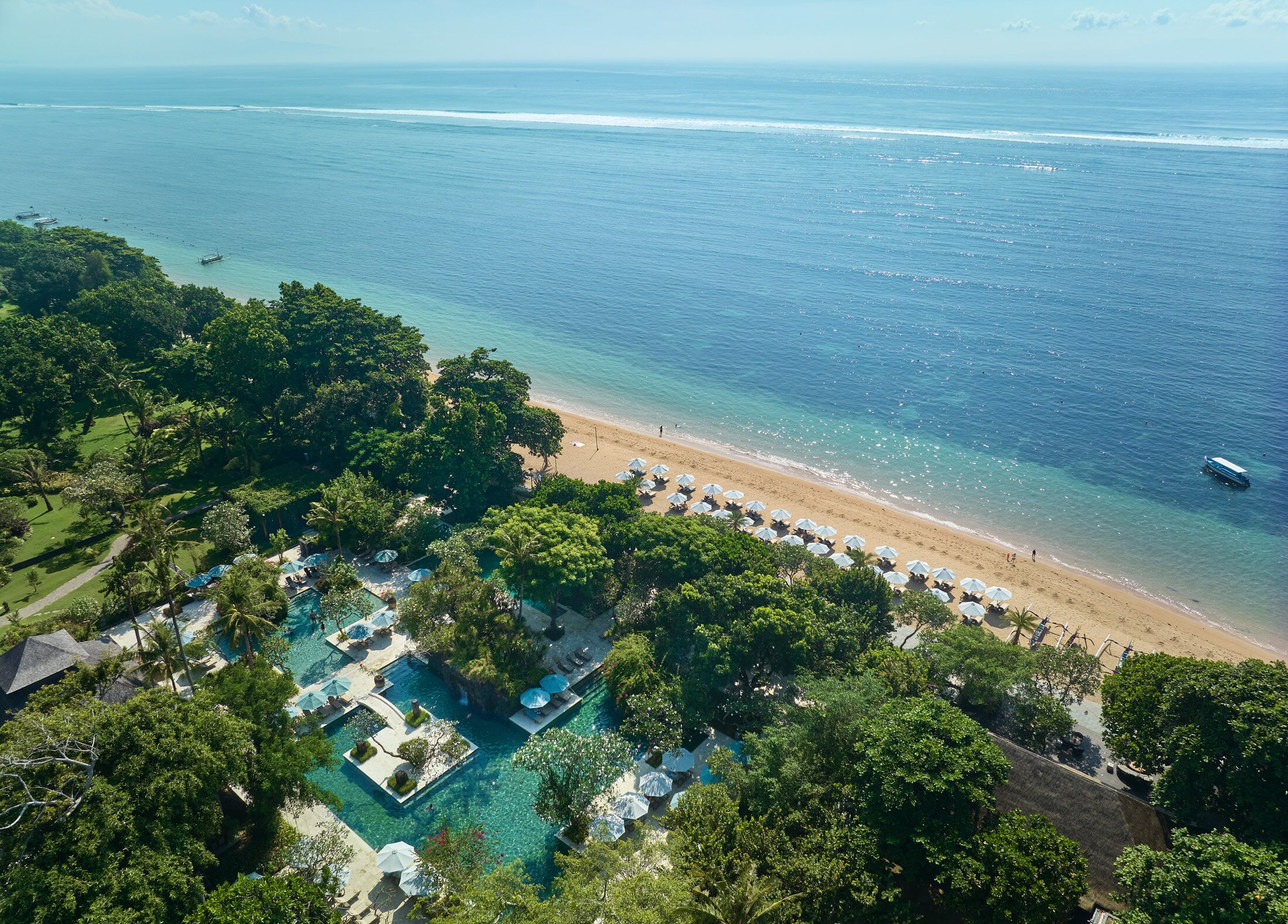 Tropu kūrorts ar peldbaseiniem un smilšu pludmali, kas stiepjas gar mierīgu okeānu, ko ieskauj zaļumi un saulītes. Ideāla vieta atpūtai un relaksācijai. panoramic view with beach and pools