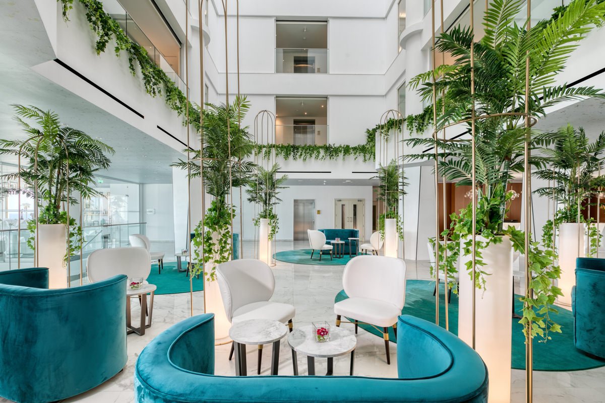 Mūsdienīgs interjers ar zaļām augiem un elegantiem mēbeļu komplektiem, radot relaksējošu atmosfēru. Šis dizains apvieno stilu un komfortu, piedāvājot ideālu vietu atpūtai.
