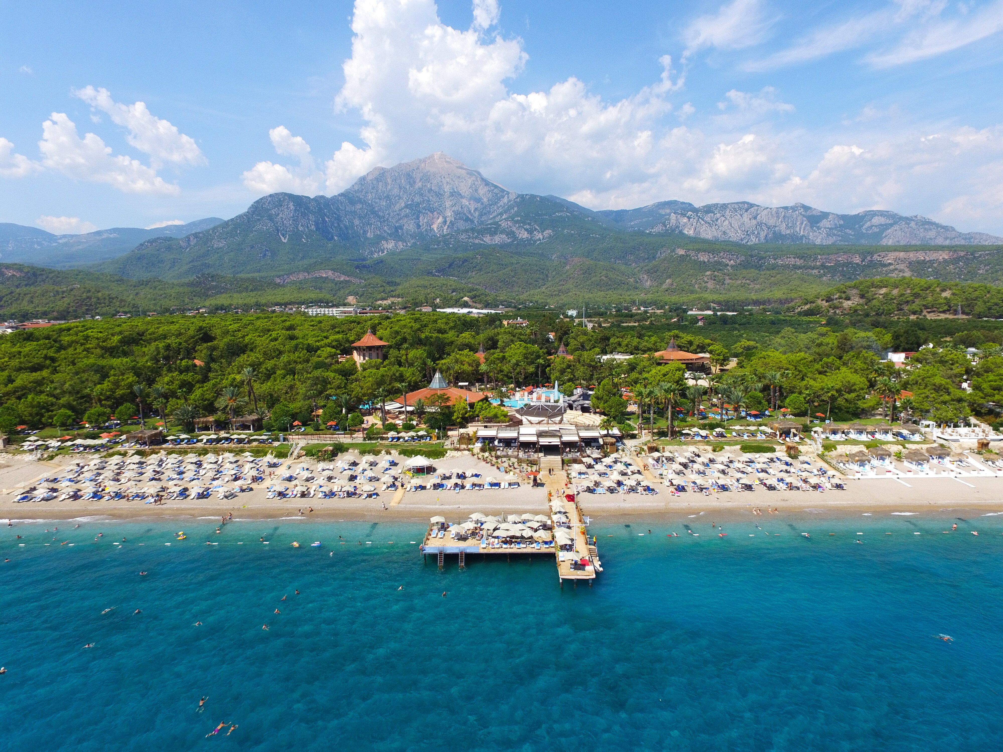 Skaista pludmales ainava ar zilu ūdeni, saules gultām un viesnīcām, kas ierīkotas pie krasta, apkārt kalni un zaļa daba. panoramic view with beach and pools