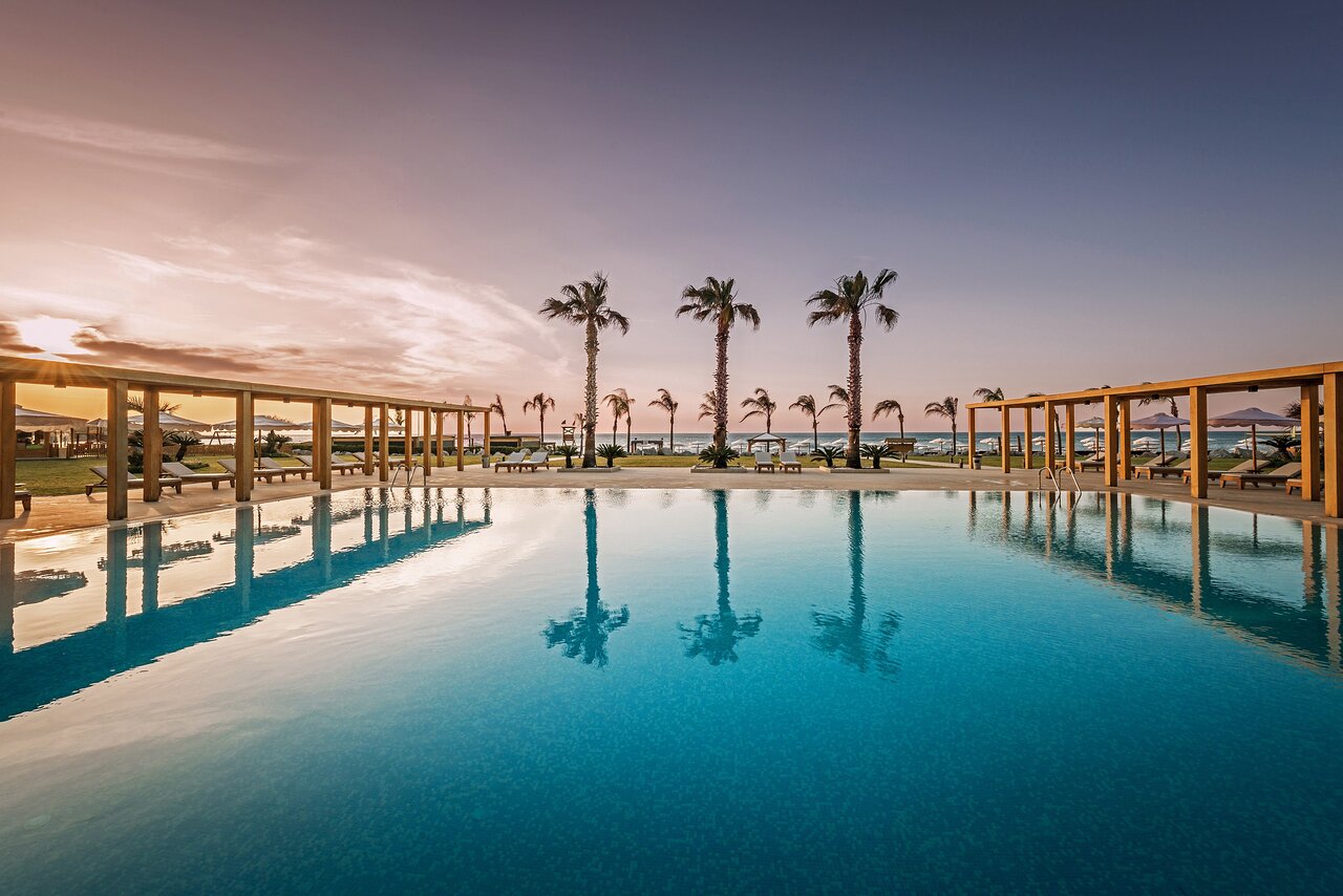 Tropu viesnīcas baseins ar palmām un saulrietu fona, radot relaksējošu atmosfēru. Ideāla vieta atpūtai un brīvdienām. panoramic view with beach and pools