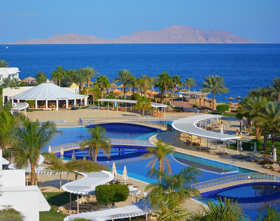 Vasaras kūrorts ar baseiniem un palmām, redzams zils jūras skats un kalni tālumā. Ideāla vieta atpūtai un relaksācijai. panoramic view with beach and pools