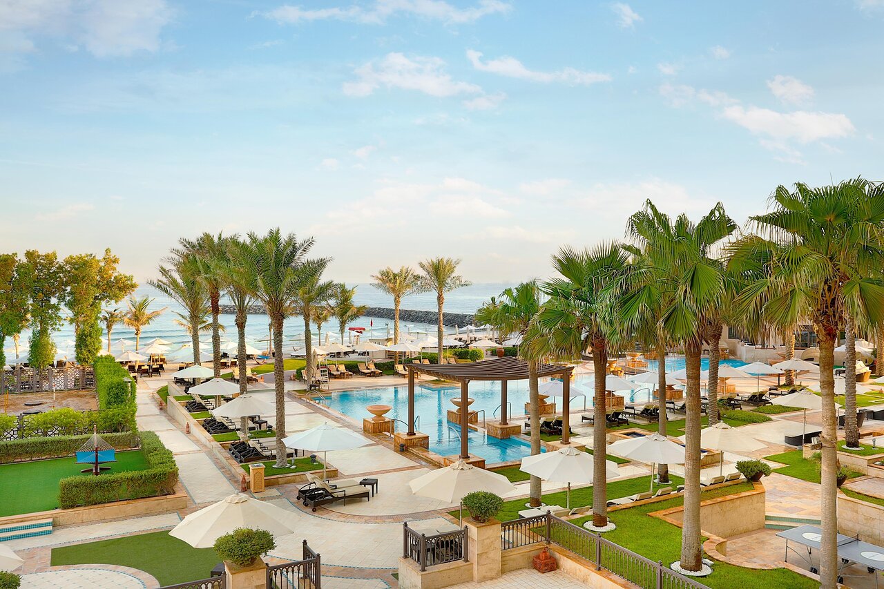 Vēlaina viesnīcas terase ar palmām un peldbaseinu, kas atrodas blakus pludmalei. Apskatāma saulaina debess un mierīga jūra. panoramic view with beach and pools