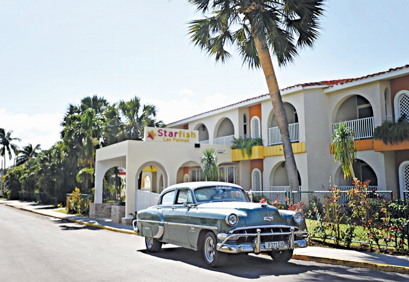 Vintage Chevrolet automobilis priekšā viesnīcai "Starfish Las Palmas", apzaļumota iela ar palmām un ziediem. panoramic view with beach and pools