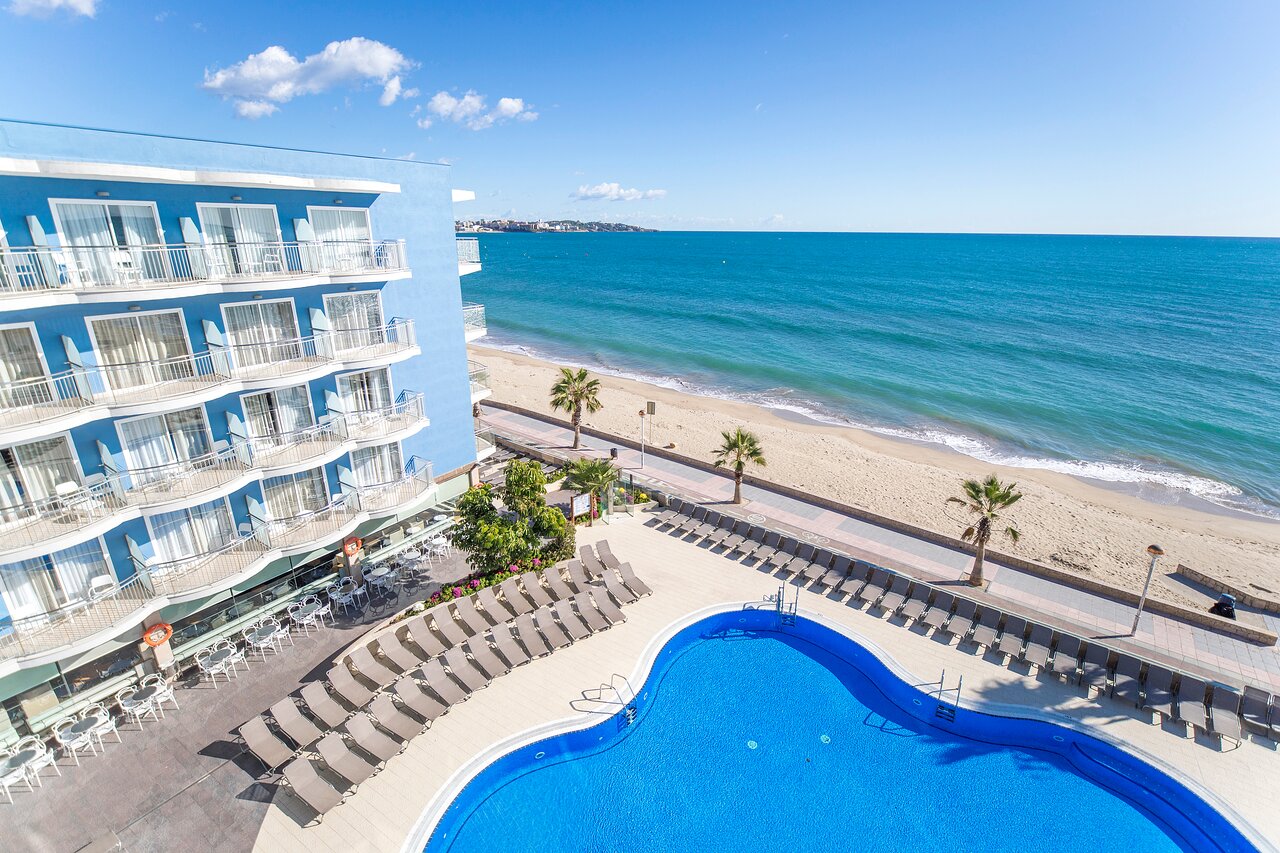 Baseina zona ar palmām, viesnīca ar zilām sienām un jūra fona, rada mierīgu atpūtas atmosfēru. Ideāla vieta atpūtai pie pludmales. panoramic view with beach and pools
