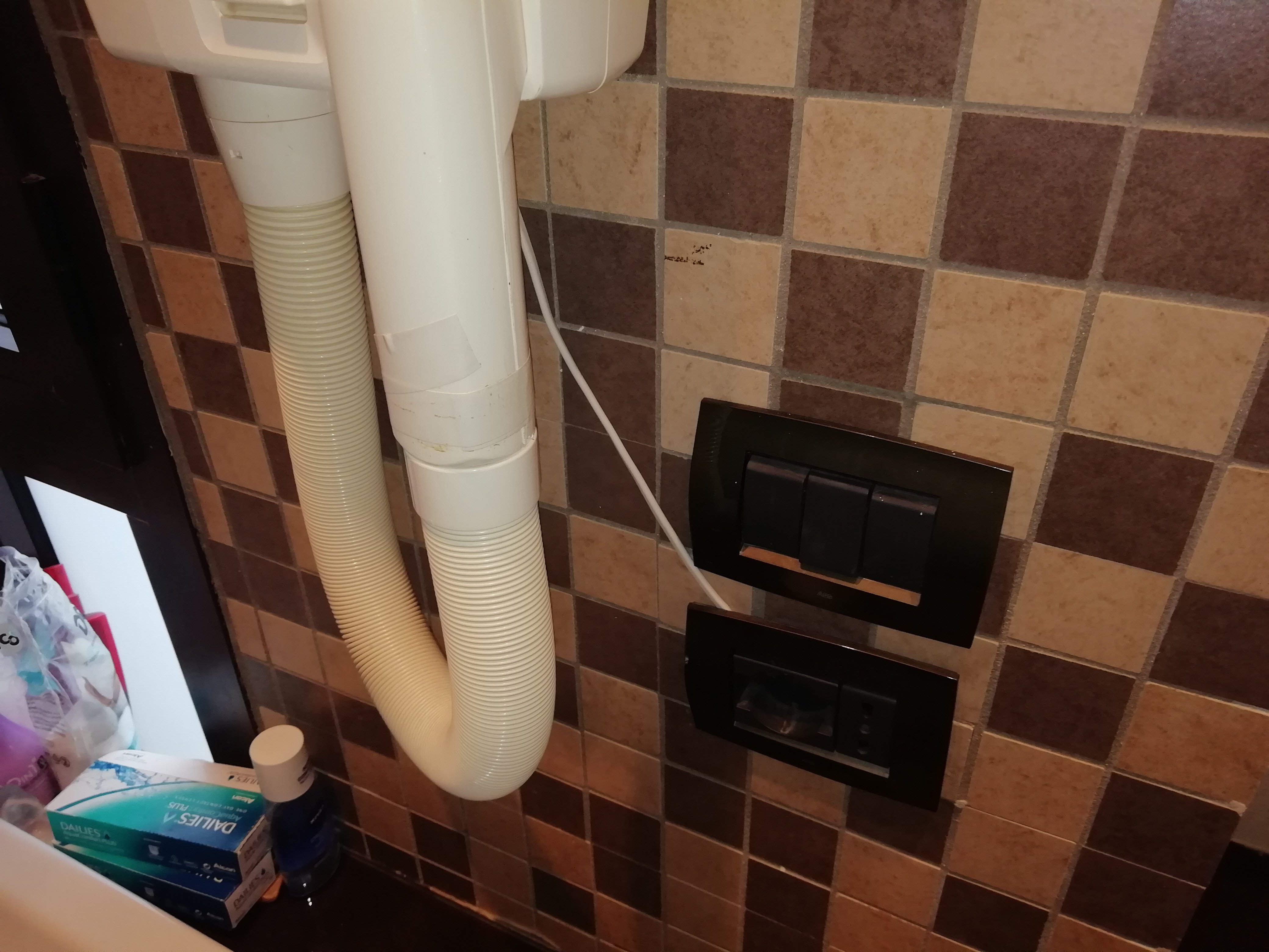 Sienas flīzes ar elektrības slēdžiem un cauruli, kas savienota ar ierīci. Šī ainava rāda ikdienas dzīves elementus.