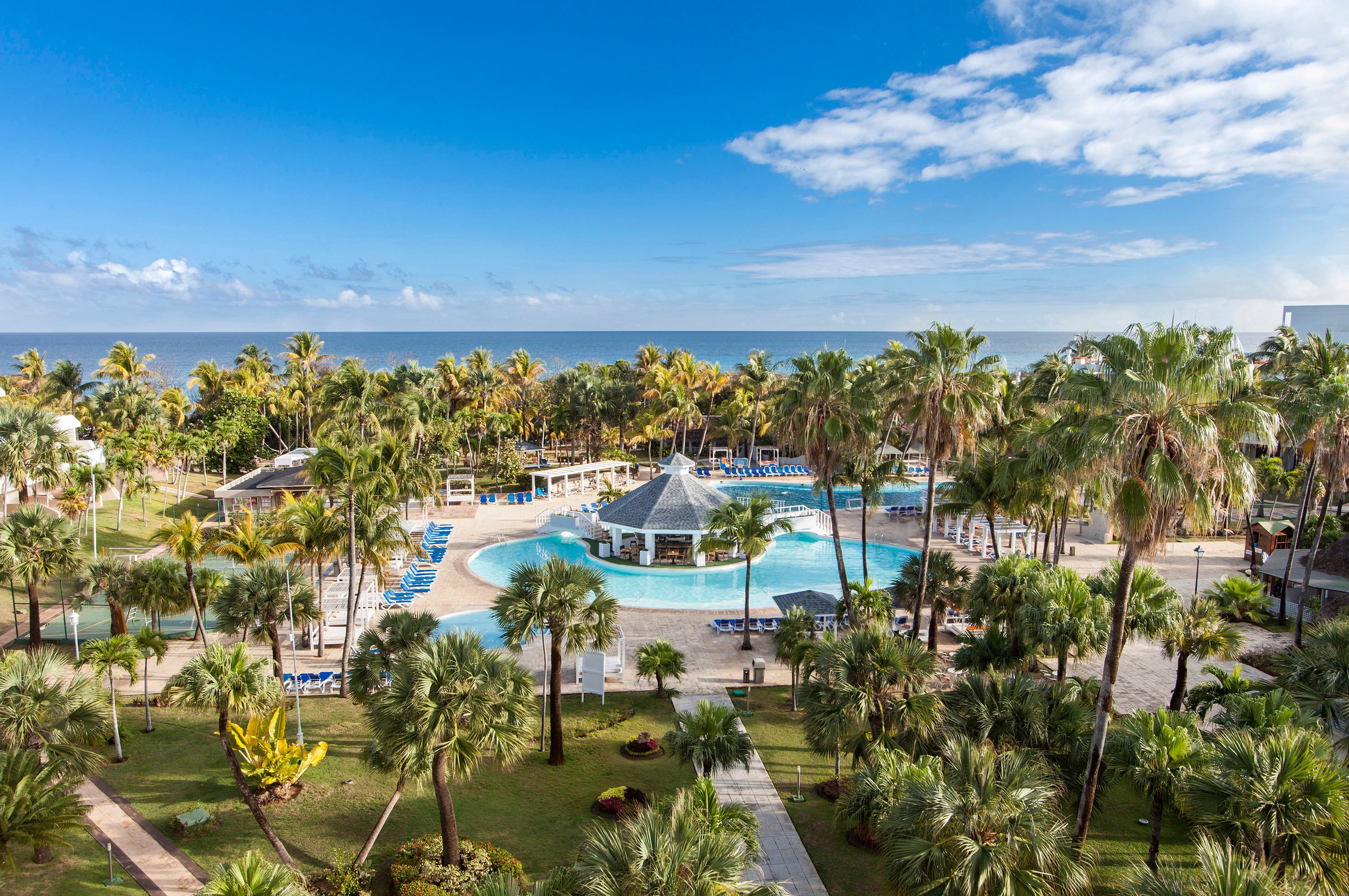 Tropu kūrorts ar peldbaseinu un palmu ainavu, kas stiepjas līdz jūrai un skaidrām debesīm. Ideāla vieta relaksācijai un atpūtai. panoramic view with beach and pools